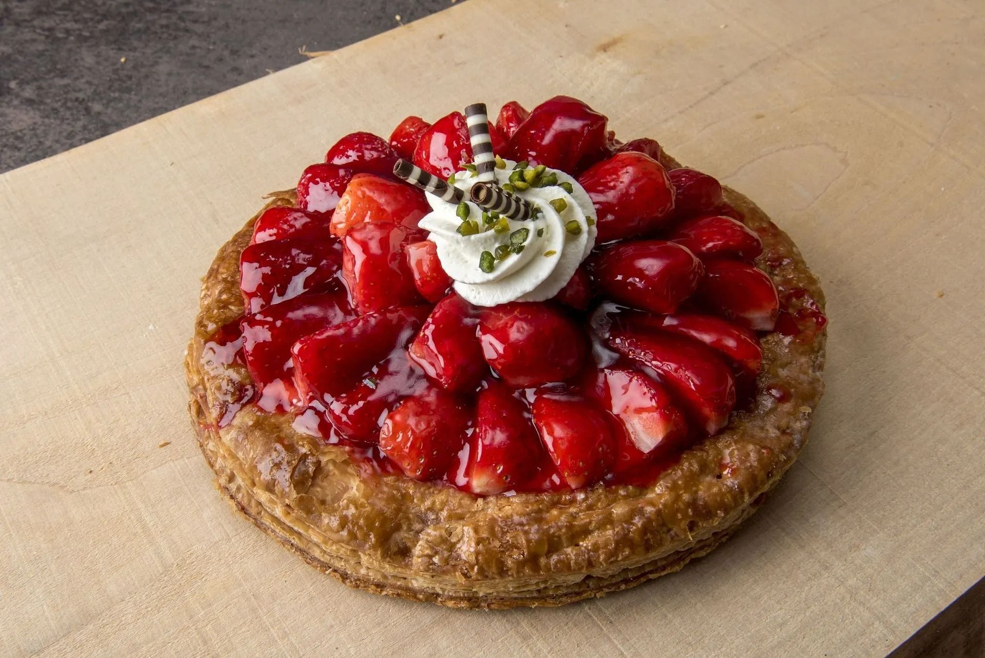 Tarte aux fraises avec crème fouettée et chocolat sur une planche en bois.