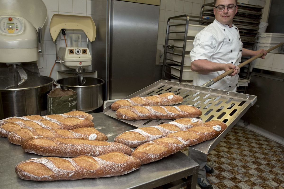 Boulanger avec des baguettes fraîches, utilisant une pelle pour les retirer d'un four commercial.