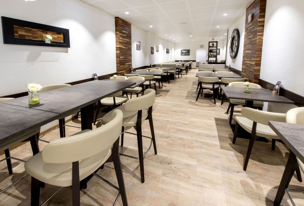 Intérieur du restaurant : longues tables, chaises crème, touches de bois, parquet en bois clair, murs blancs.