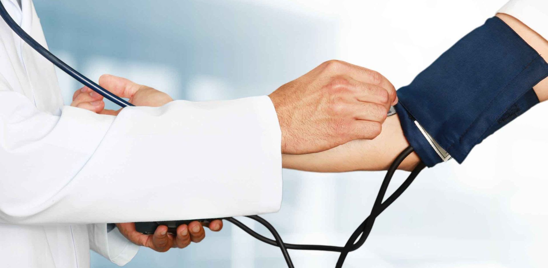 Manos sujetando un brazo mientras se coloca un manguito de presión arterial, con un estetoscopio visible en un entorno médico.