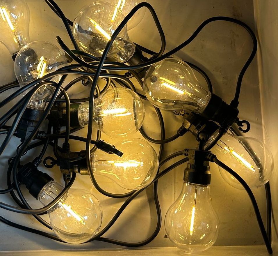 Guirlande d'ampoules claires de style Edison allumées et emmêlées sur un fond blanc.