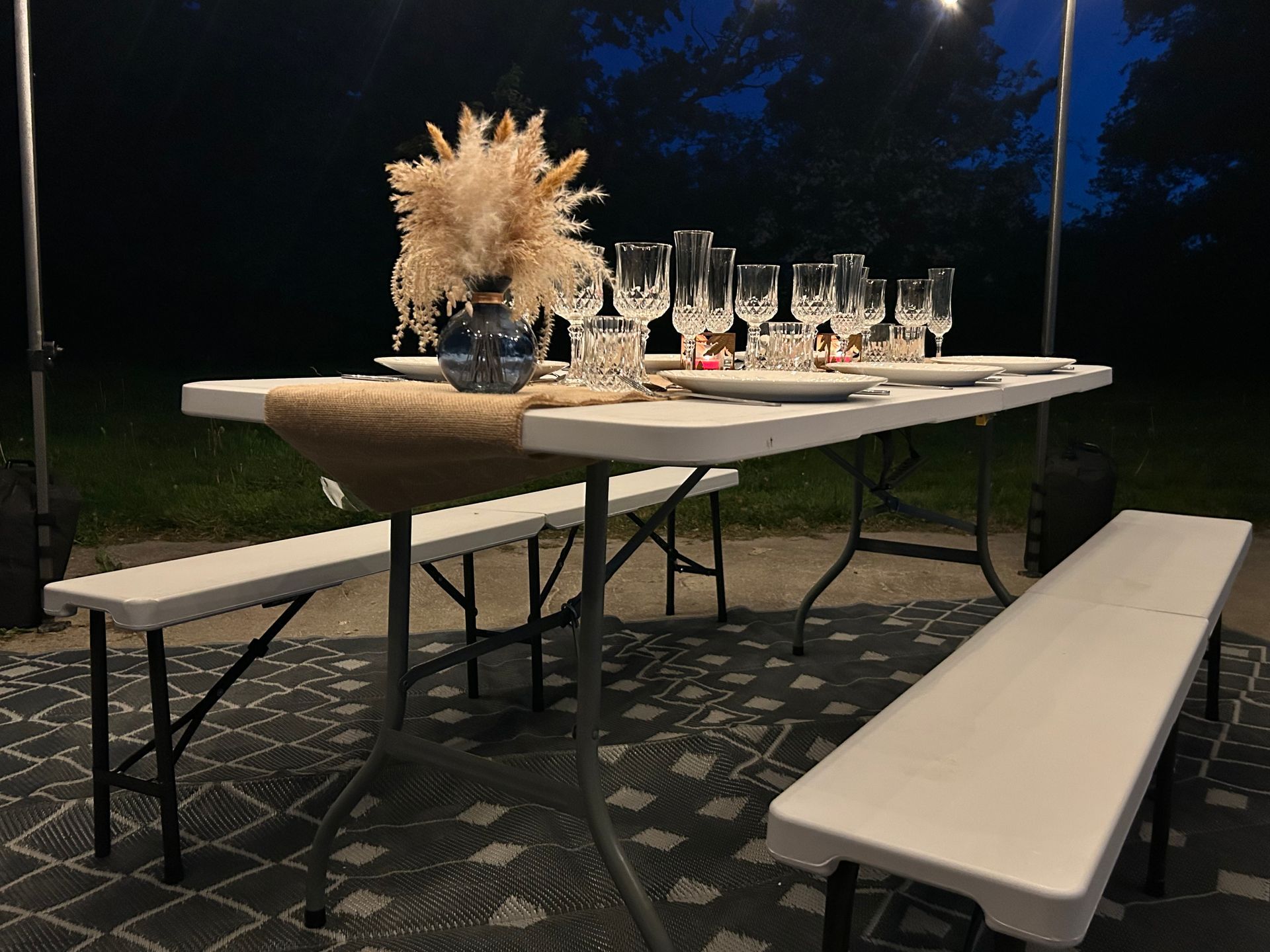 Table et banc blancs avec verres et assiettes posés sur la table agrémentée d'un bouquet de fleurs