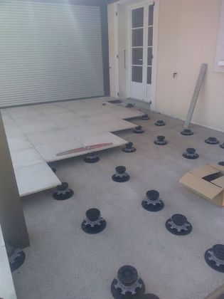 Terrasse extérieure avec dalles surélevées sur supports réglables, à côté d'une porte de garage fermée et d'une porte vitrée.