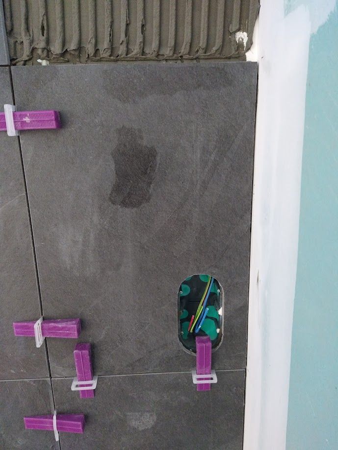 Sol carrelé gris avec des clips de nivellement violets et une cale verte près du bord d'un mur