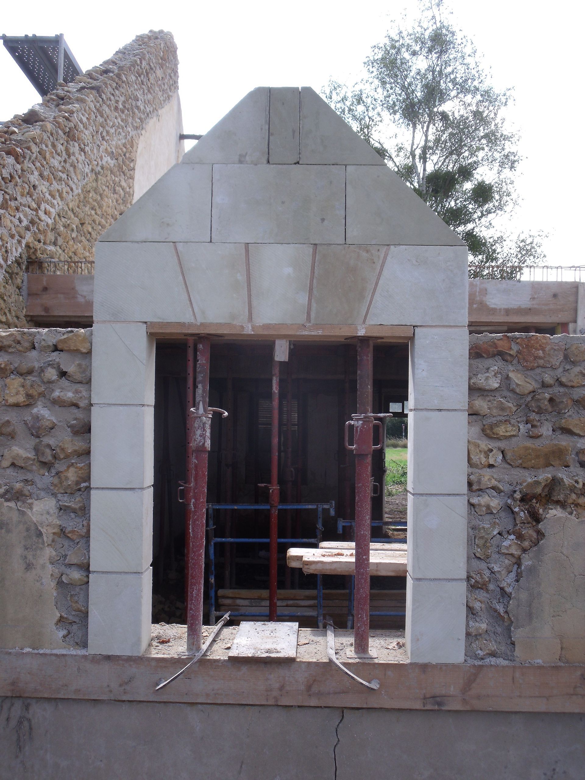 Fenêtre en pierre en construction, avec échafaudages à l'intérieur et un sommet triangulaire à gradins.