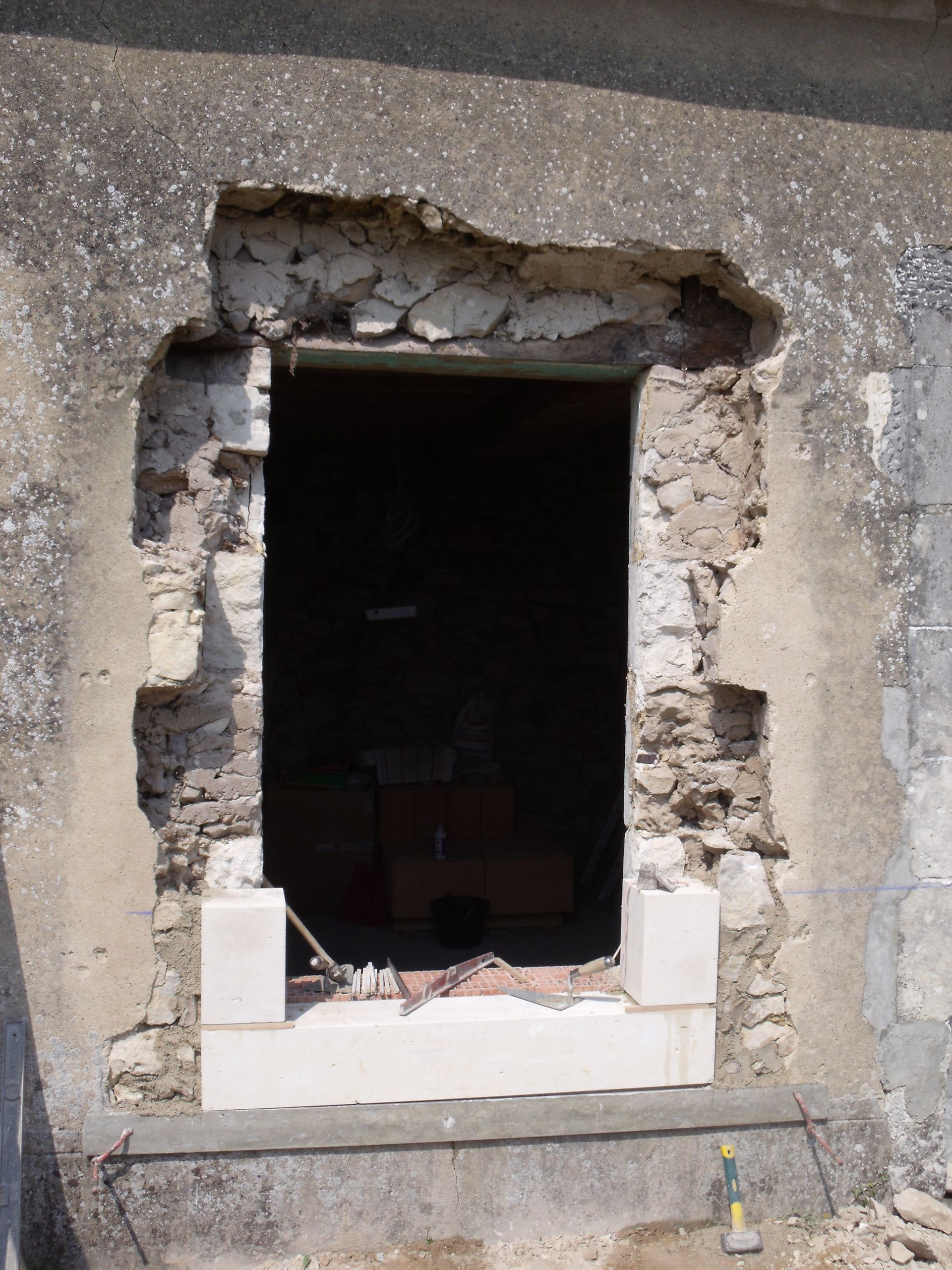 Ouverture de fenêtre brisée dans un mur en béton avec des décombres apparents autour du cadre