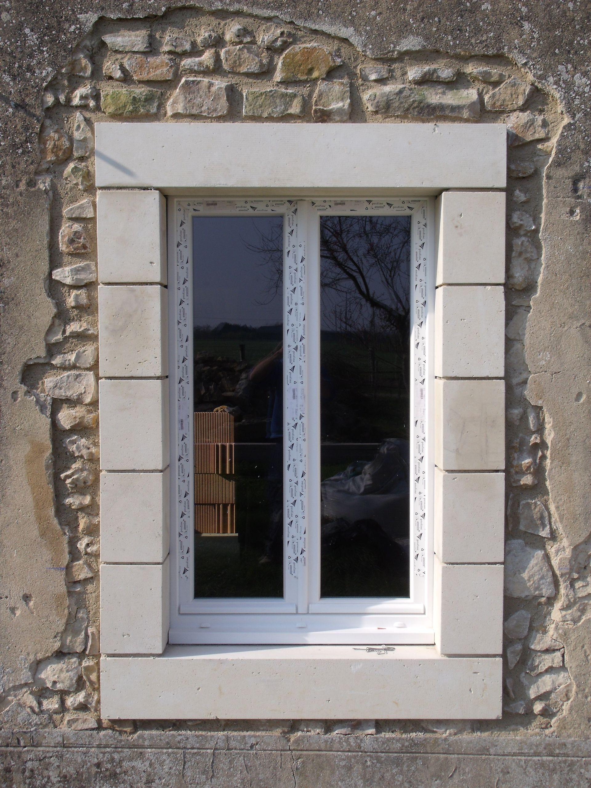 Fenêtre en pierre d'une maison, avec cadre et volets blancs reflétant l'extérieur