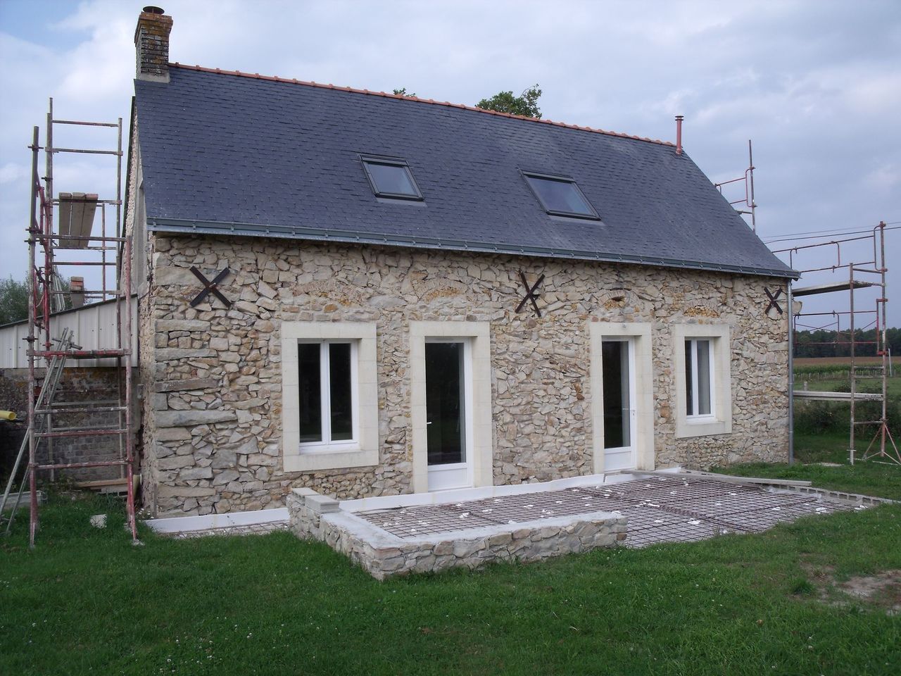 Maison en pierre en rénovation, avec échafaudages, toit sombre et fenêtres à cadre blanc