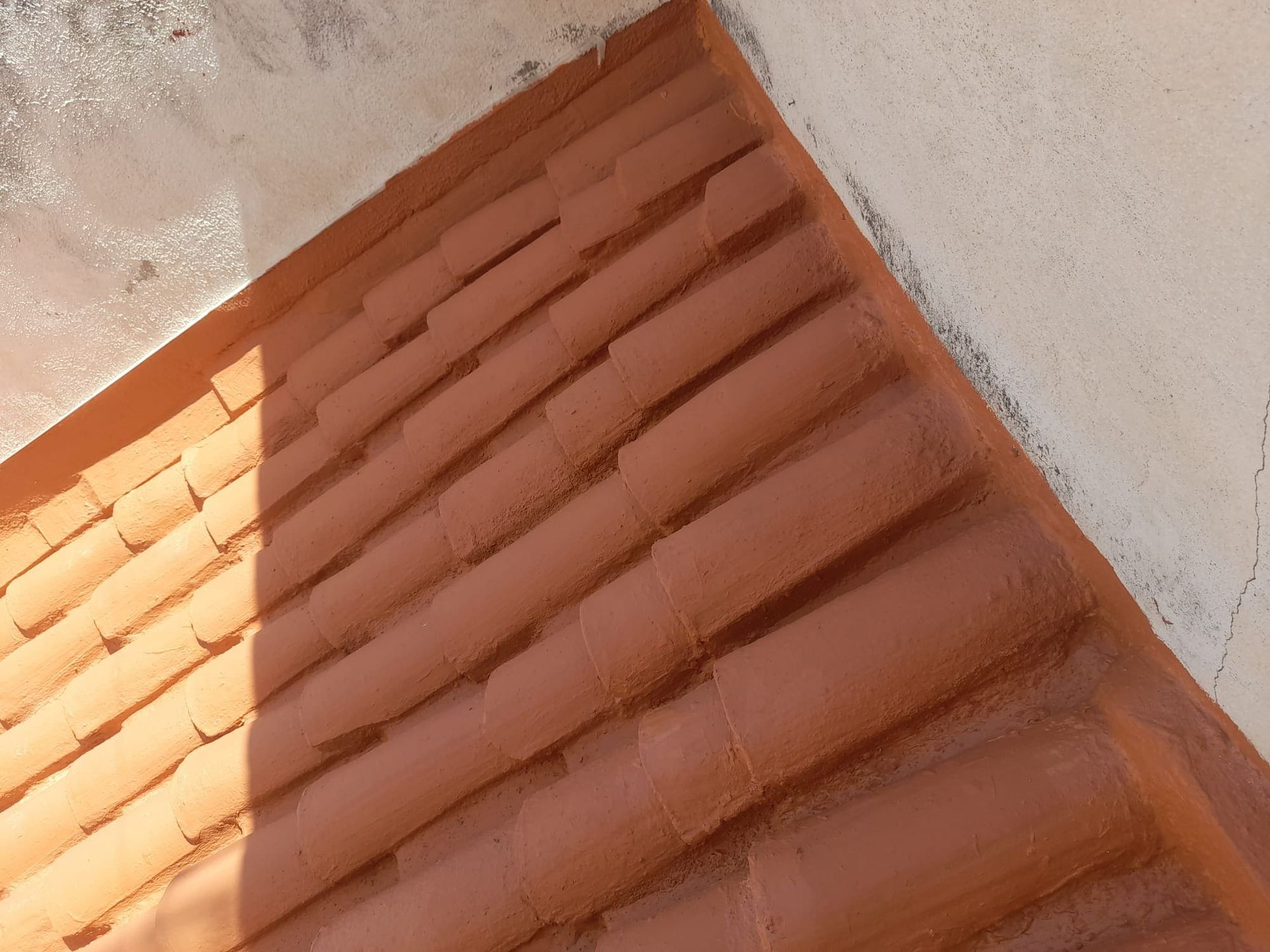 Un primer plano de un techo de tejas con una pared blanca al fondo.