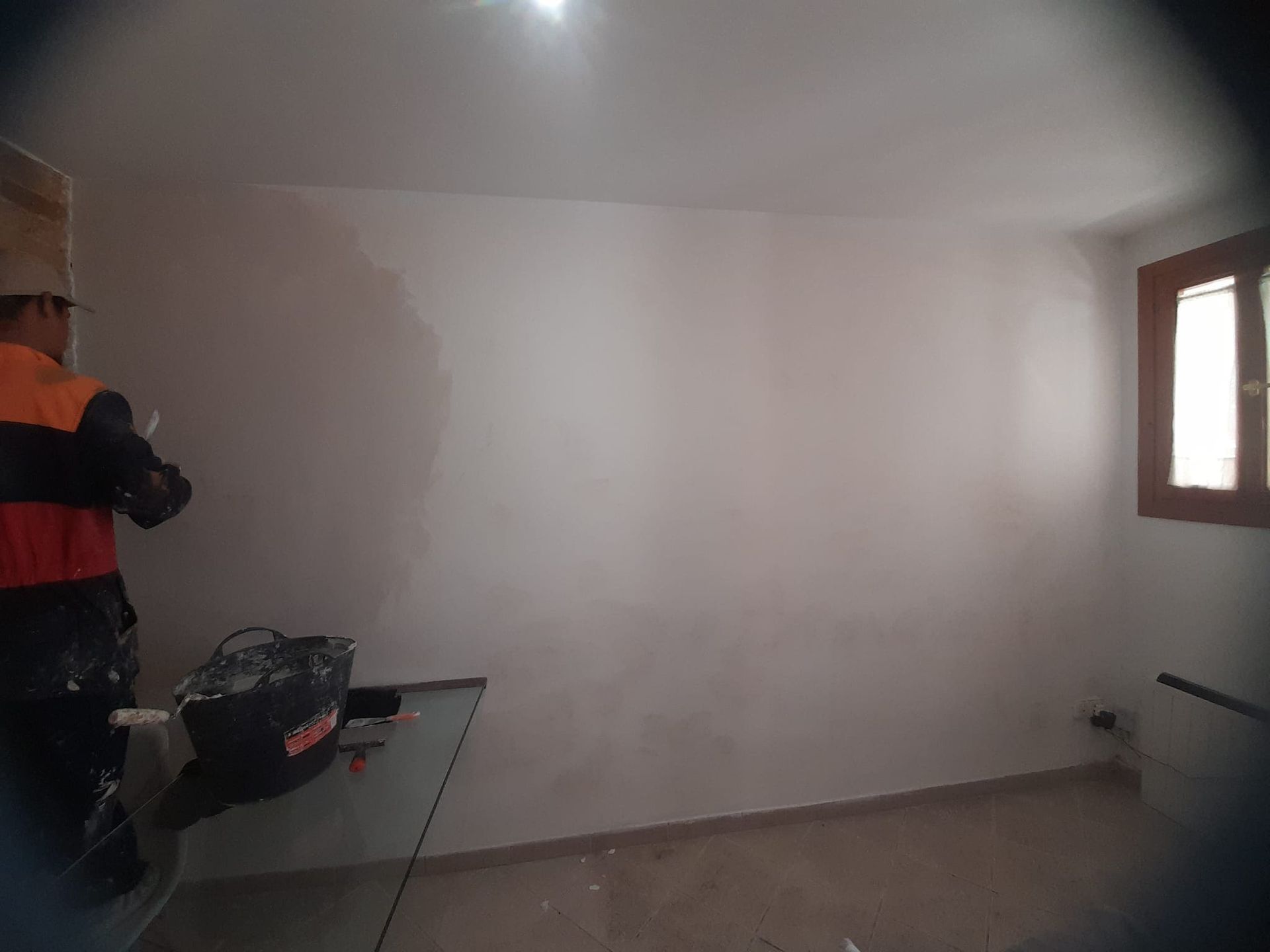 Un hombre está de pie en una habitación con una pared blanca y una ventana.