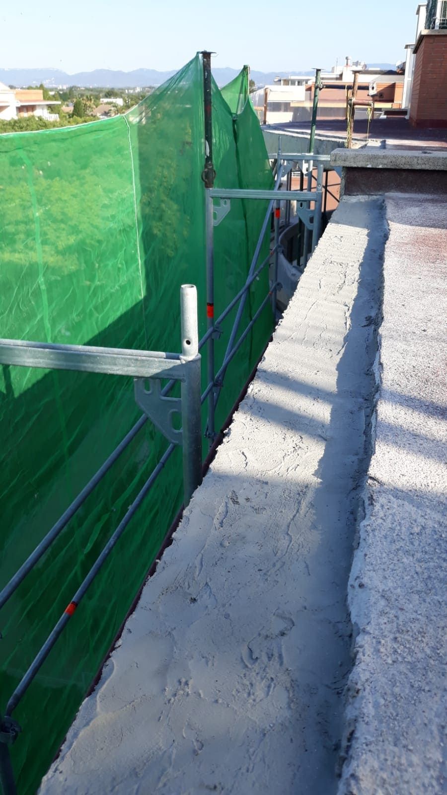 Un muro de hormigón con andamios y una red verde que lo cubre.