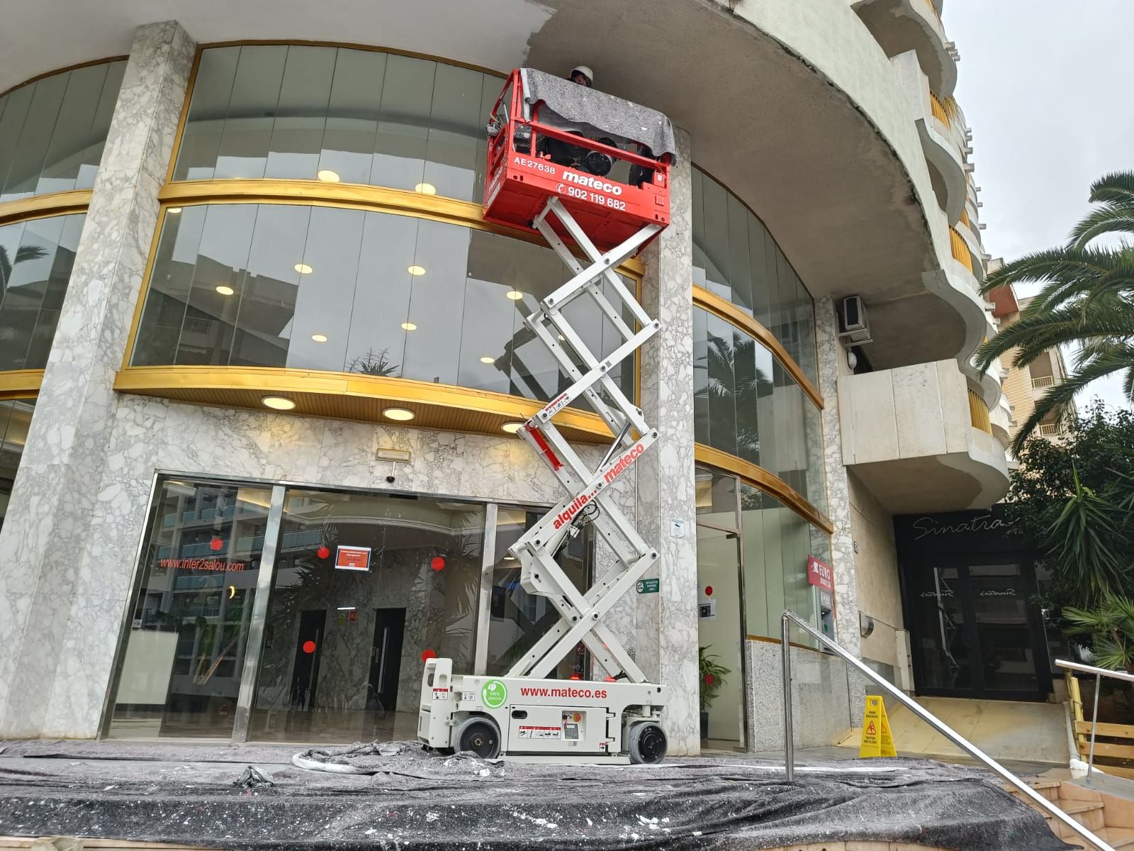 Un elevador de tijera está situado delante de un edificio.