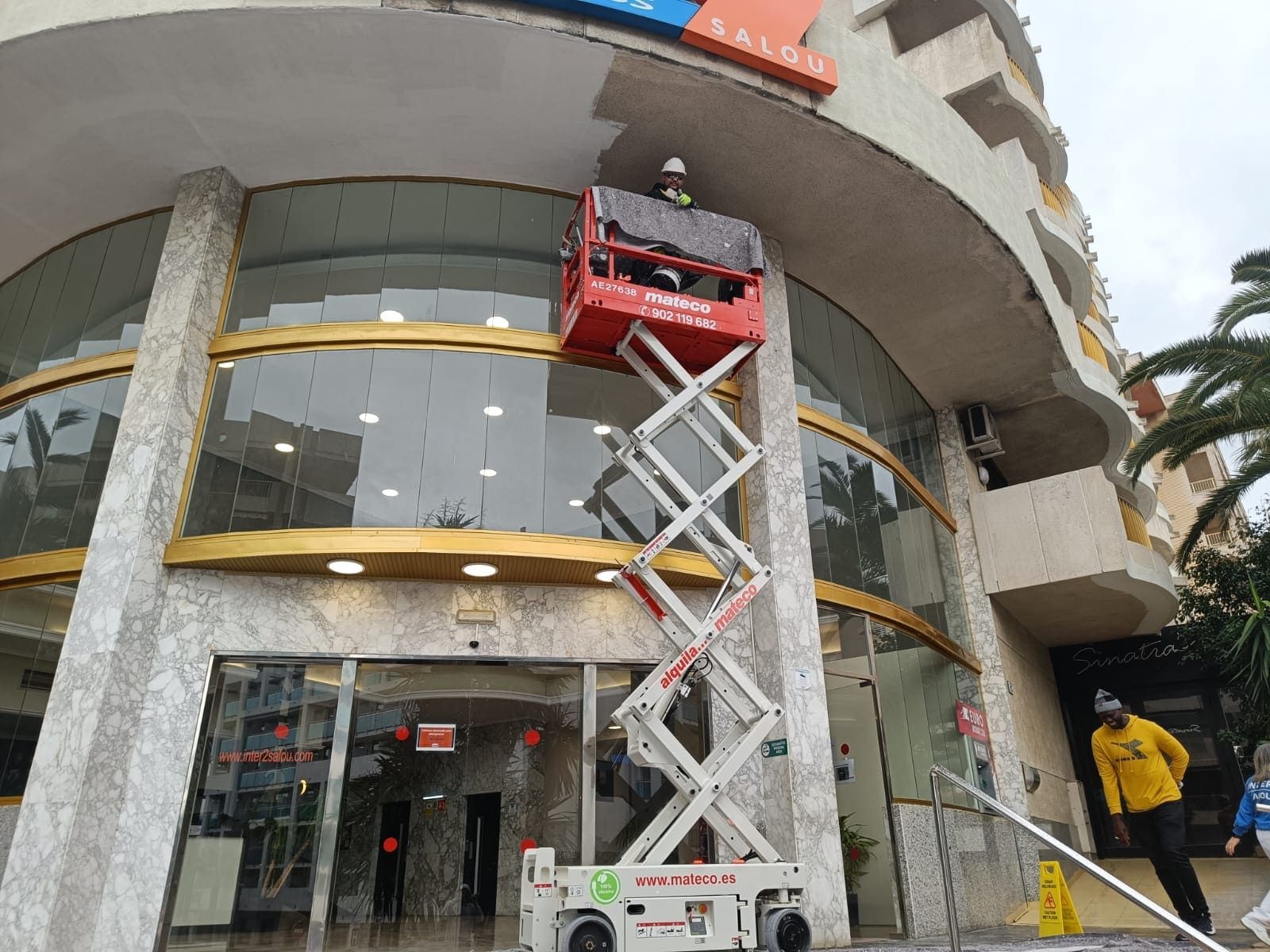 Un hombre está parado en un elevador de tijera frente a un edificio.