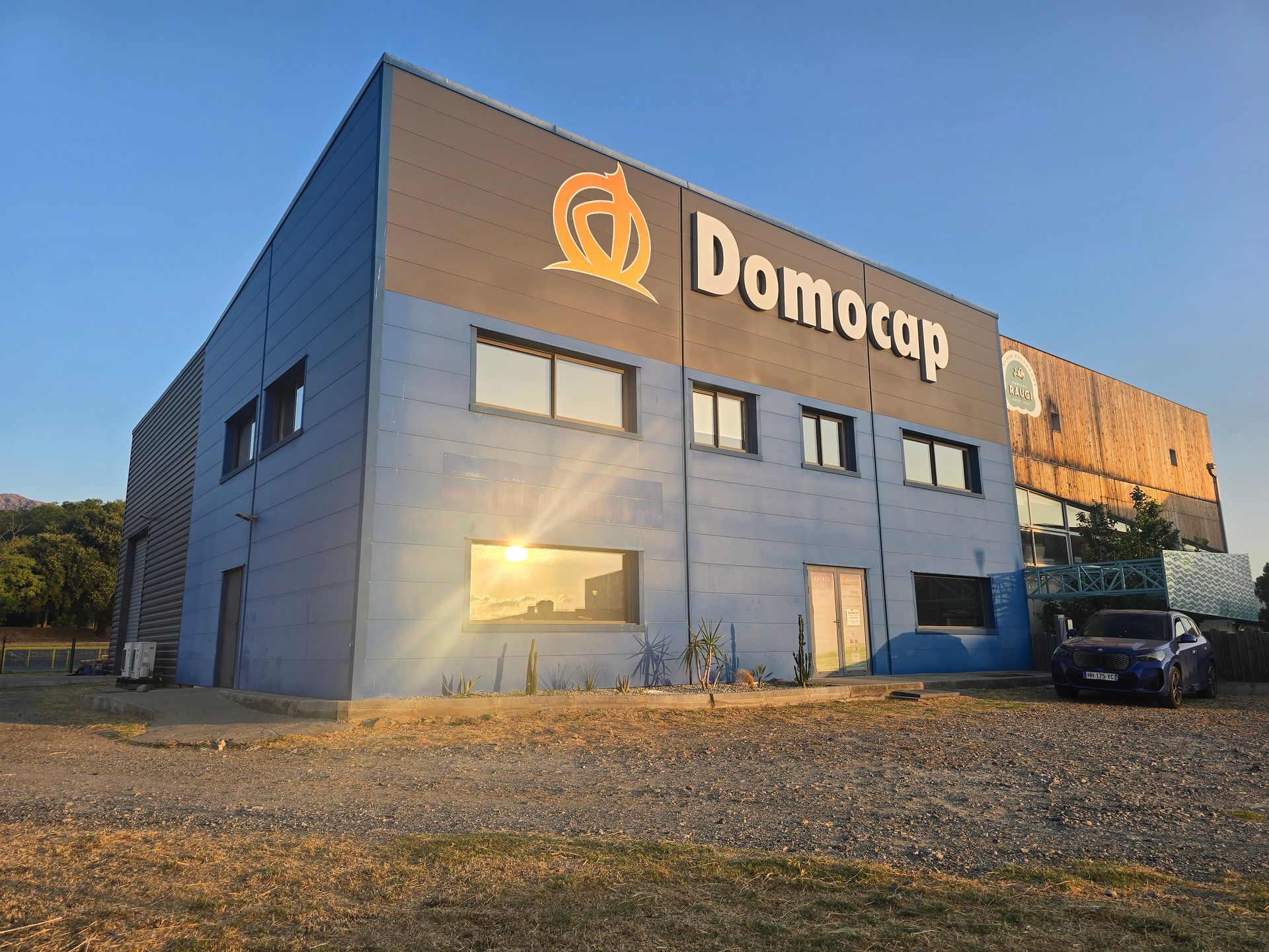 Bâtiment Domocap avec un véhicule garé devant sur un terrain en gravier