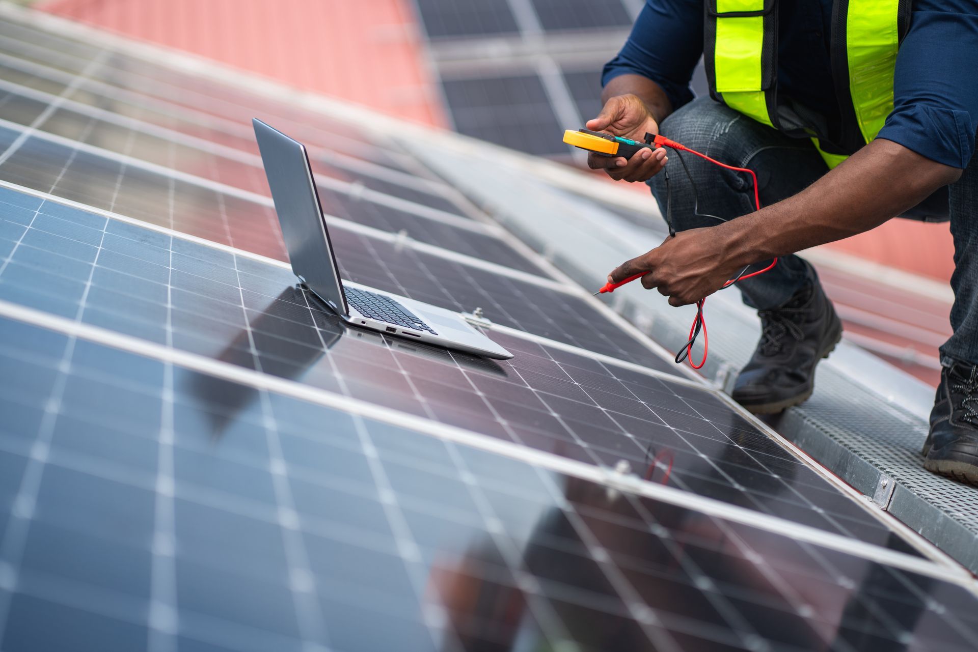 Un technicien teste des panneaux solaires installés sur le toit à l'aide d'un multimètre, tout en étant agenouillé sur le réseau.
