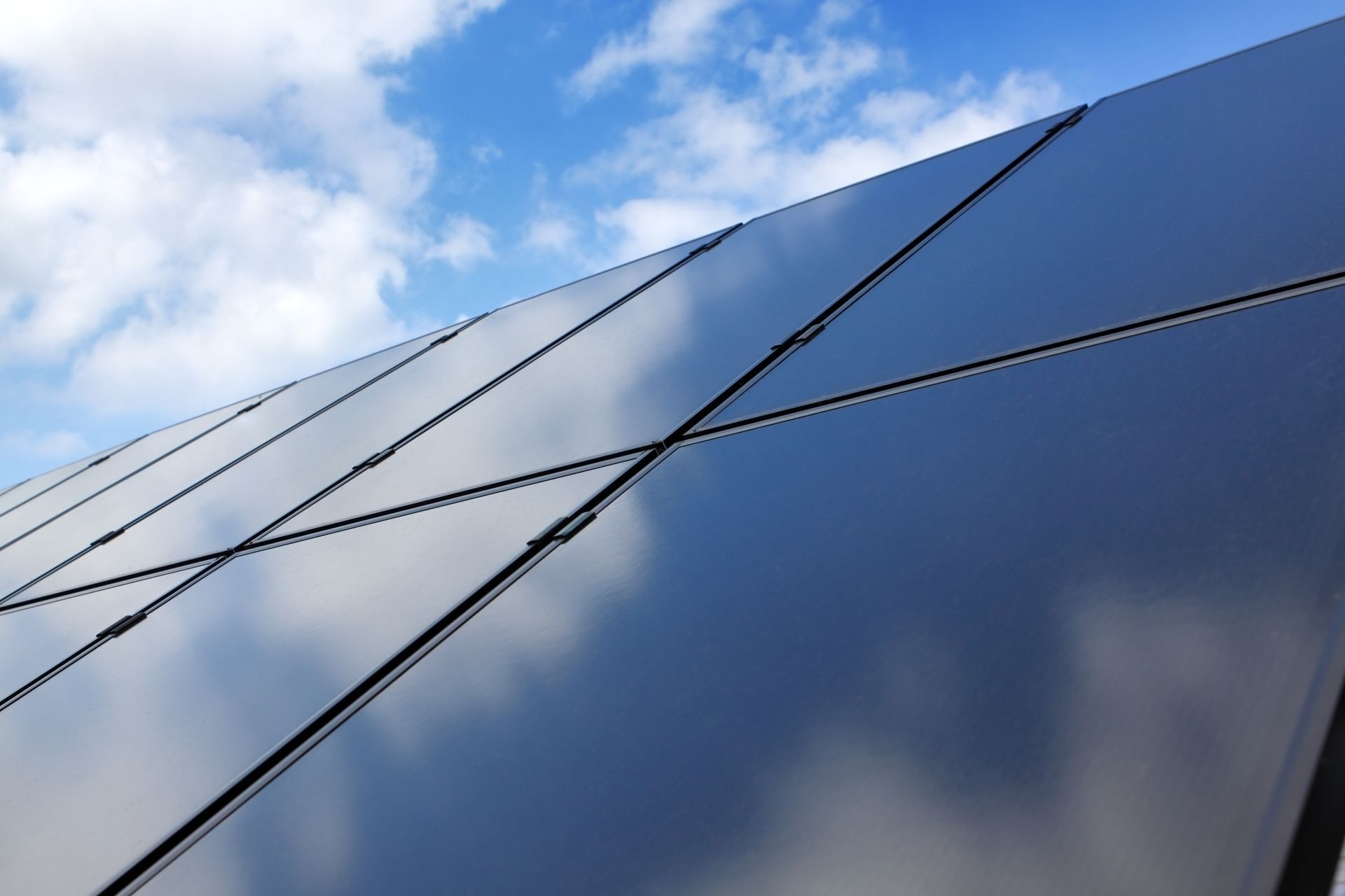 Façade d'immeuble en verre bleu réfléchissant avec des panneaux angulaires se détachant sur un ciel nuageux