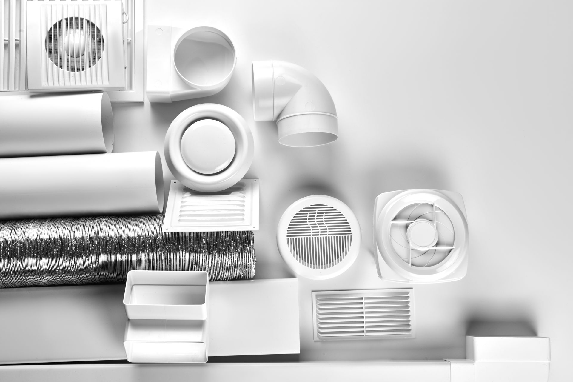 Des bouches d'aération, des conduits et des grilles de ventilation blancs et gris, soigneusement disposés sur une étagère.