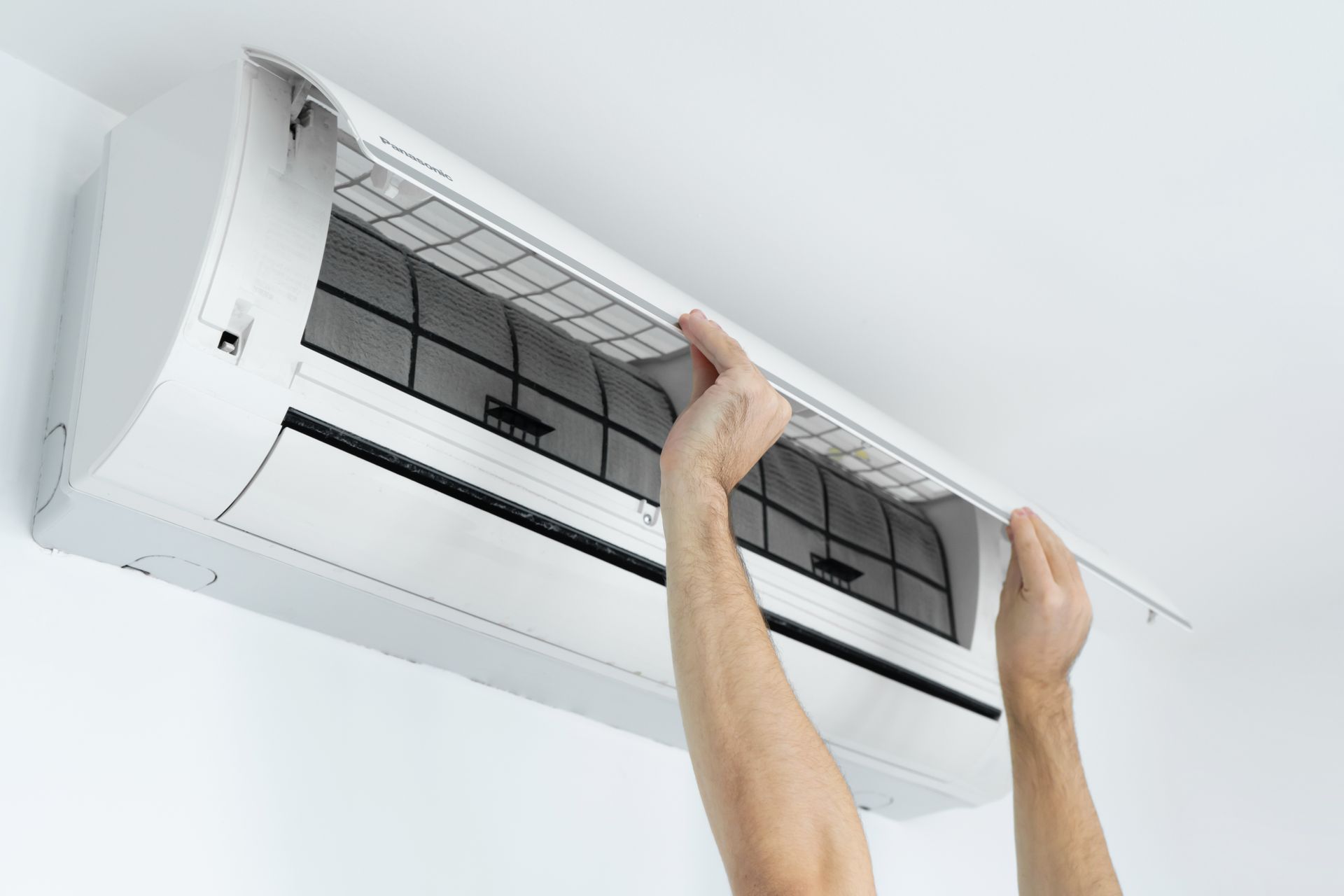 Mains nettoyant un filtre de climatiseur mural sur un plafond blanc