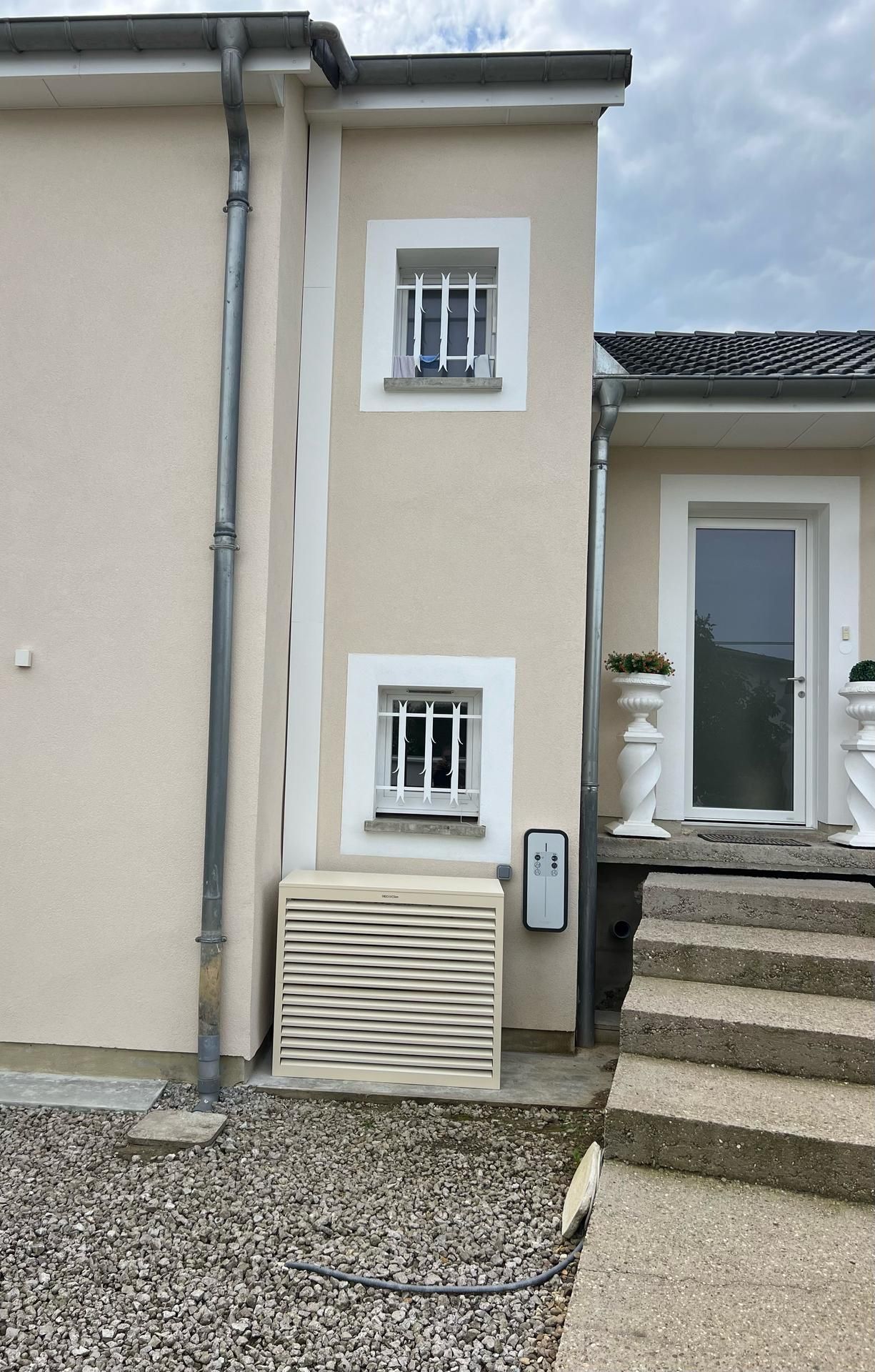 Une climatisation devant une maison beige