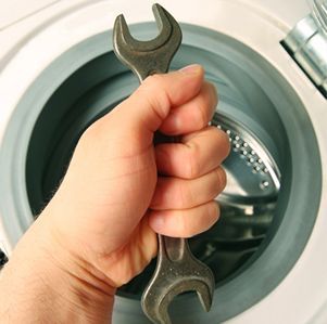 Mano sosteniendo una llave inglesa, dentro del tambor de una lavadora.