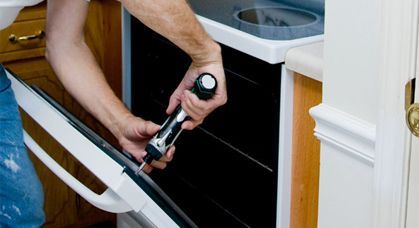 Una persona arreglando la puerta de un horno con un destornillador en una cocina.