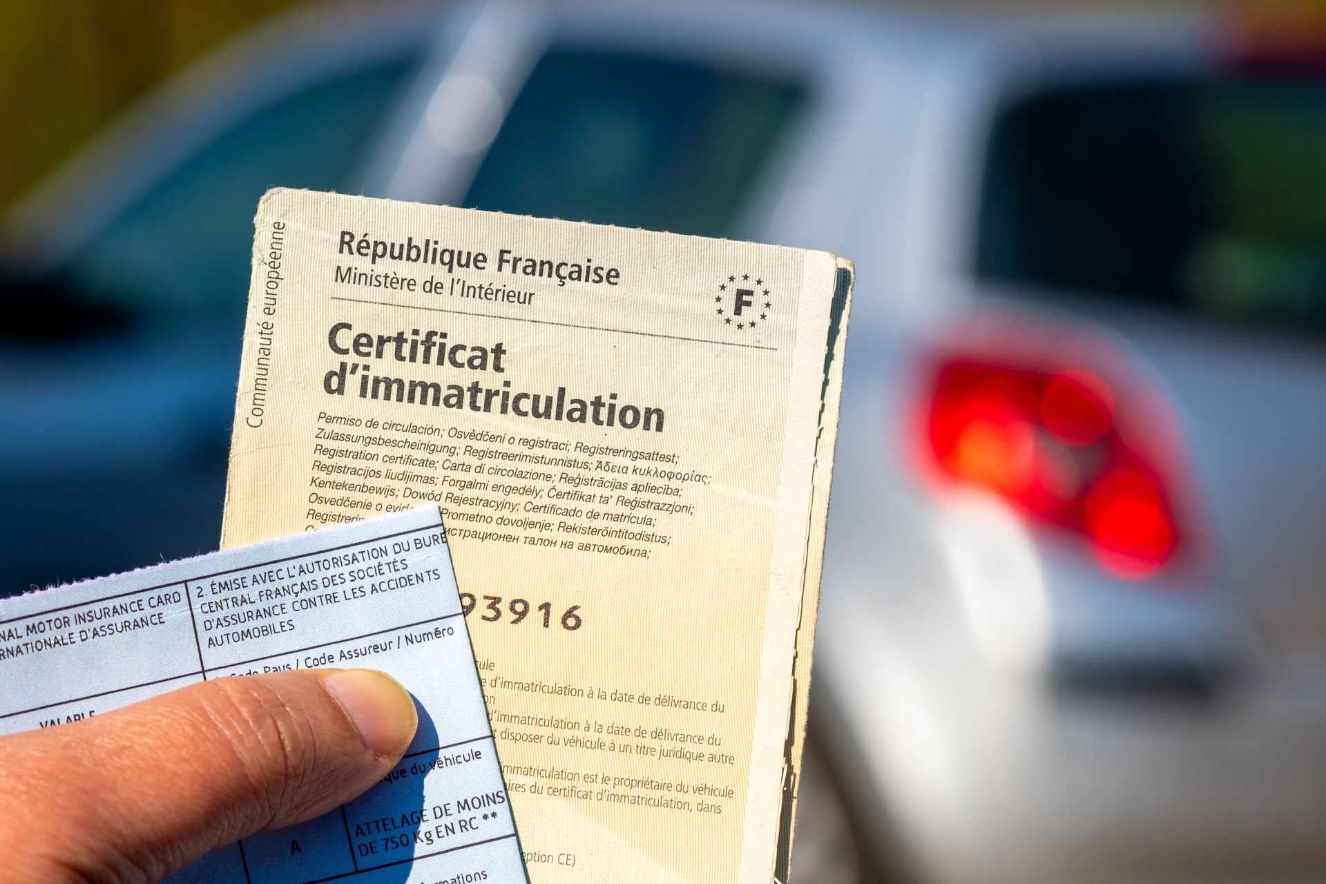 Une personne tient un certificat d'immatriculation français devant une voiture.