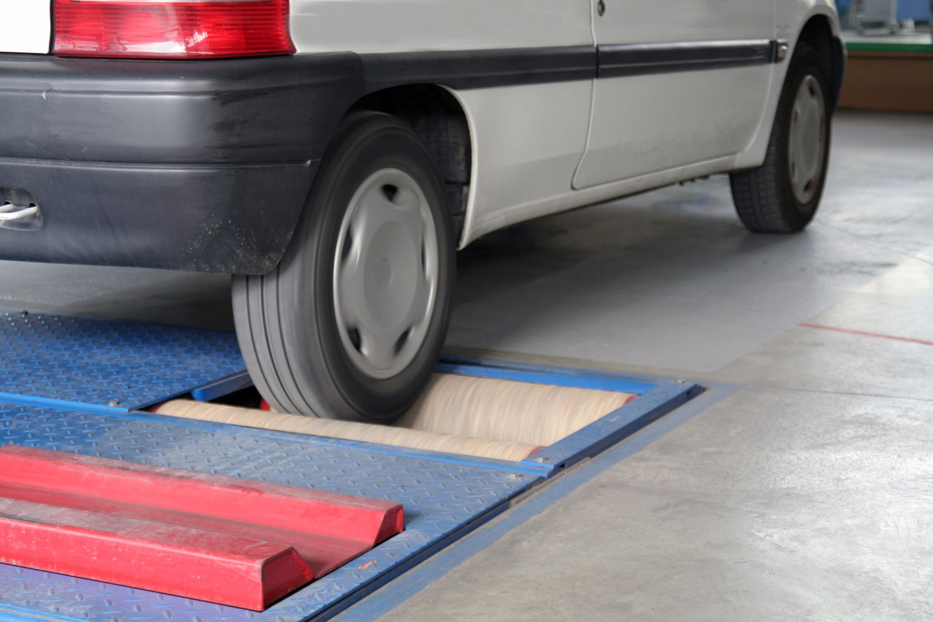 Une voiture blanche garée, sa roue arrière positionnée sur un banc d'essai de freins dans un garage.
