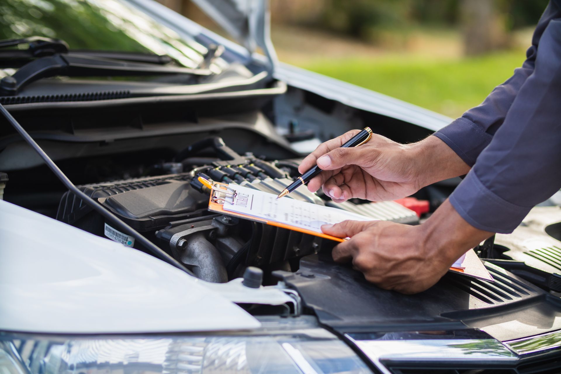 Un technicien tient un stylo et un bloc-notes tout en inspectant un moteur de voiture ouvert.
