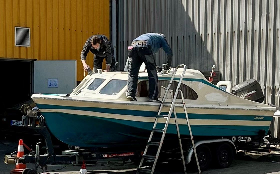 Ein Mann steht mit einem Schlauch in der Hand auf dem Deck eines Bootes.