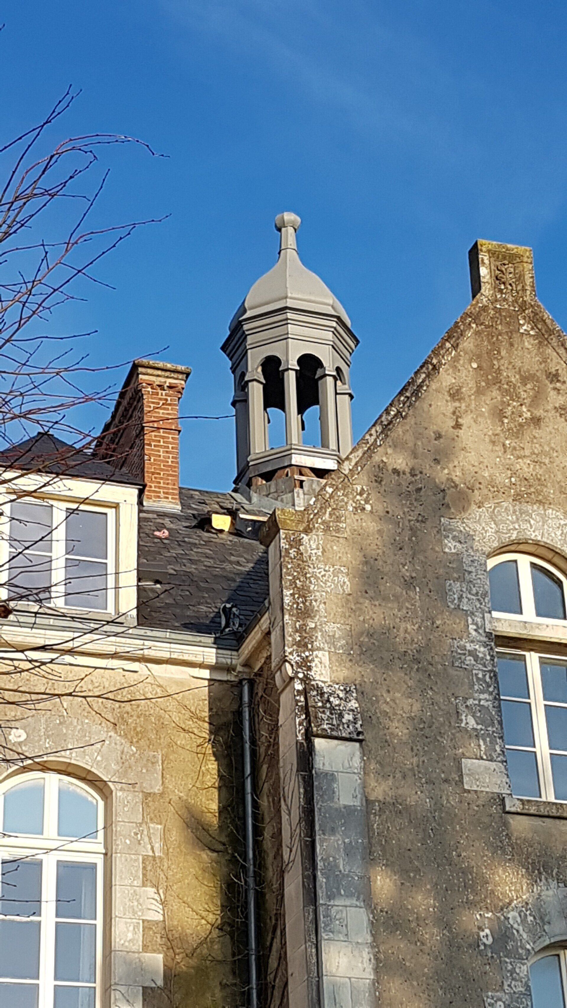 Toiture en ardoise avec une cheminée en brique, un clocheton central et une lucarne de toit