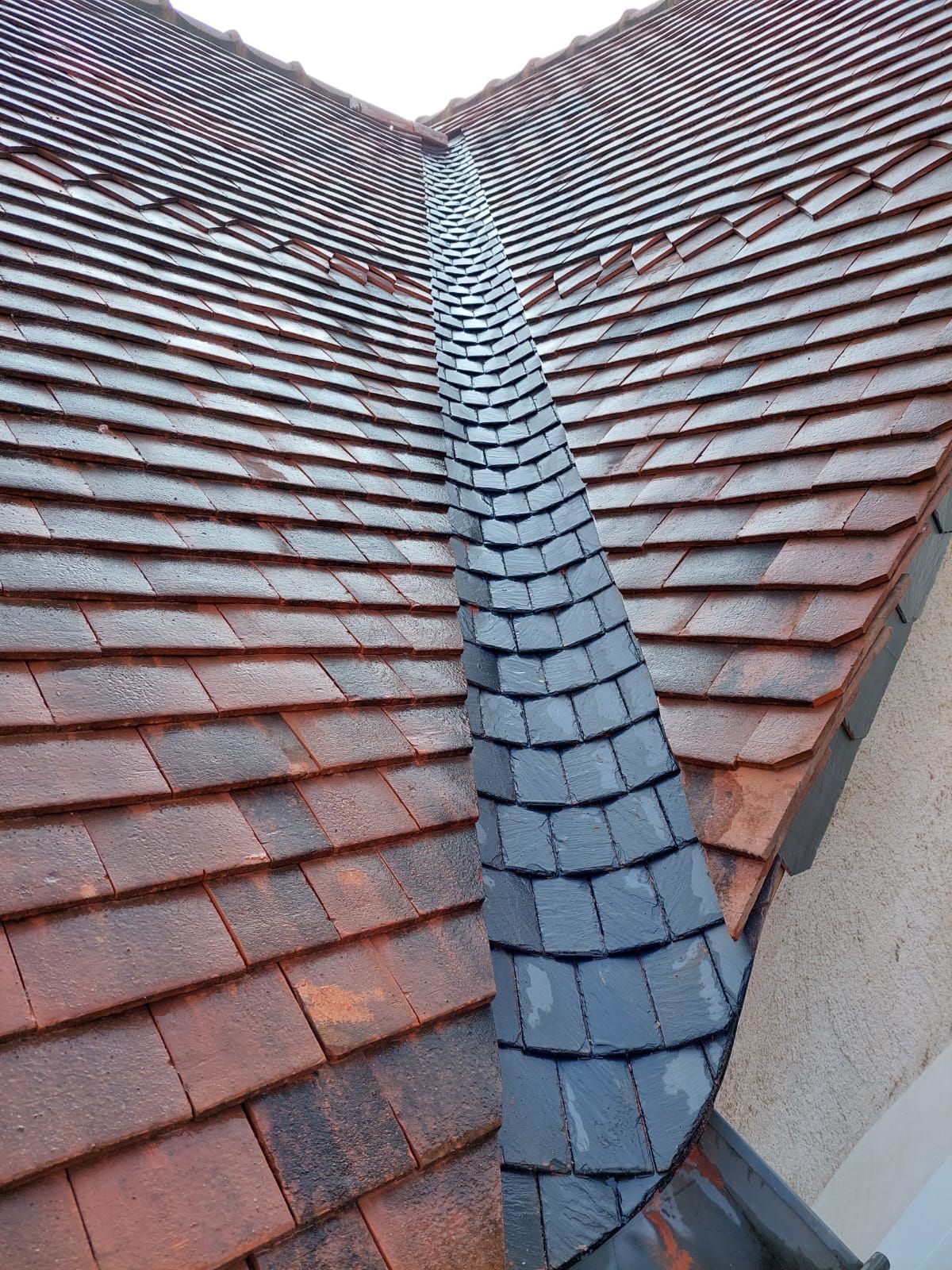 Noue de toiture en ardoise sur une toiture en tuiles rouges