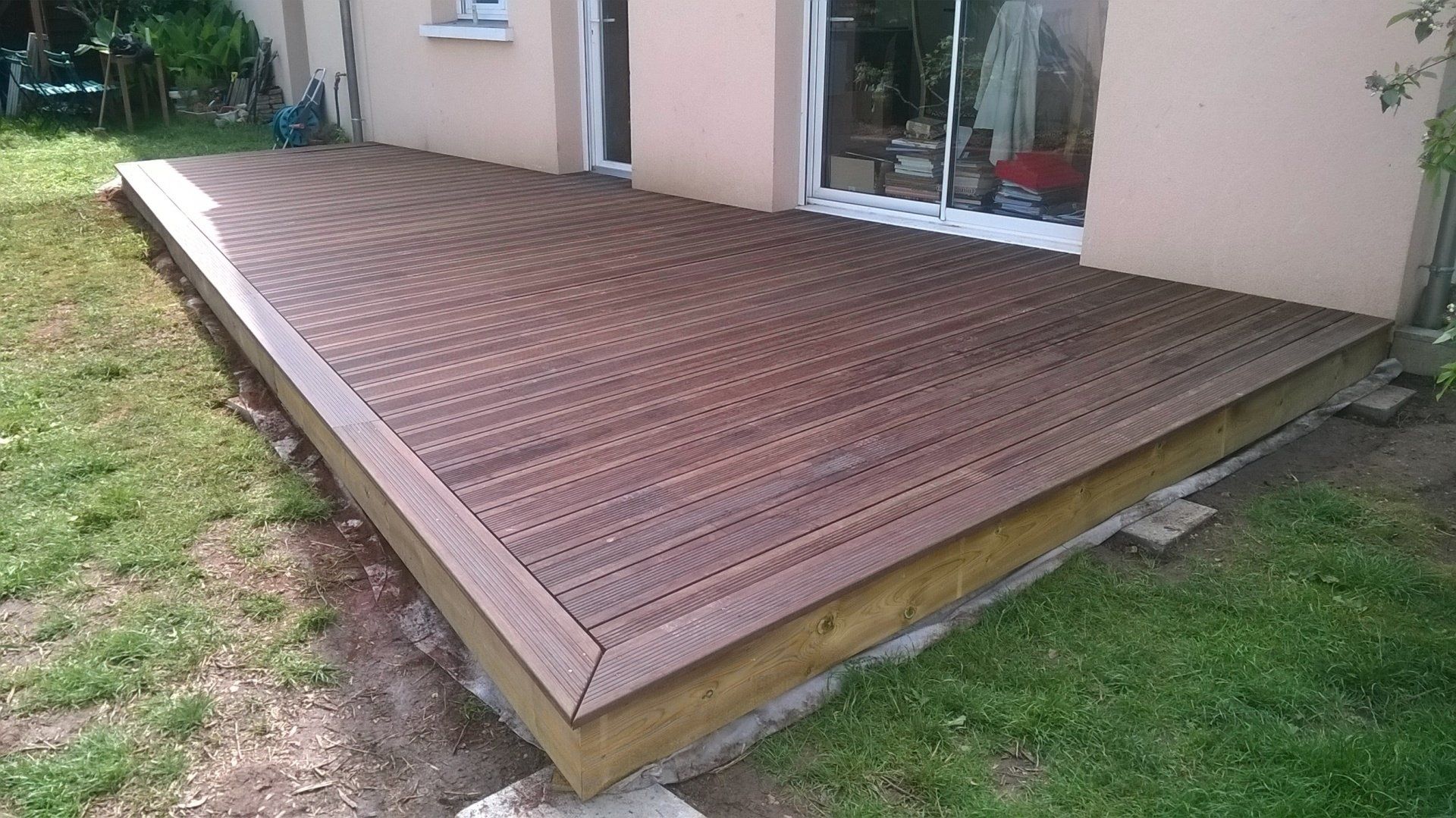 Terrasse en bois foncé terminé devant la baie vitrée d'une maison
