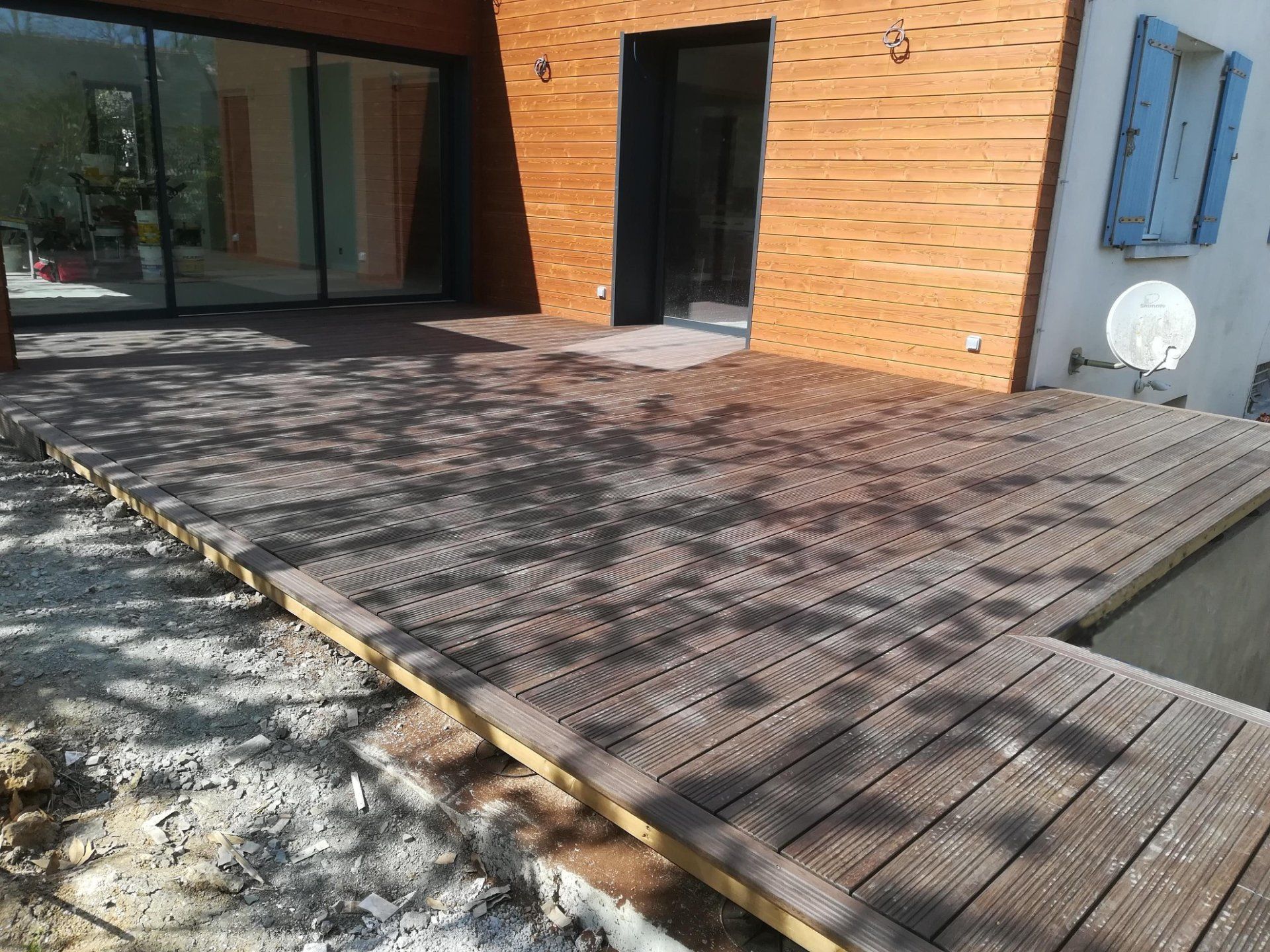 Terrasse en bois terminée avec baie vitrée et entrée d'une maison au fond