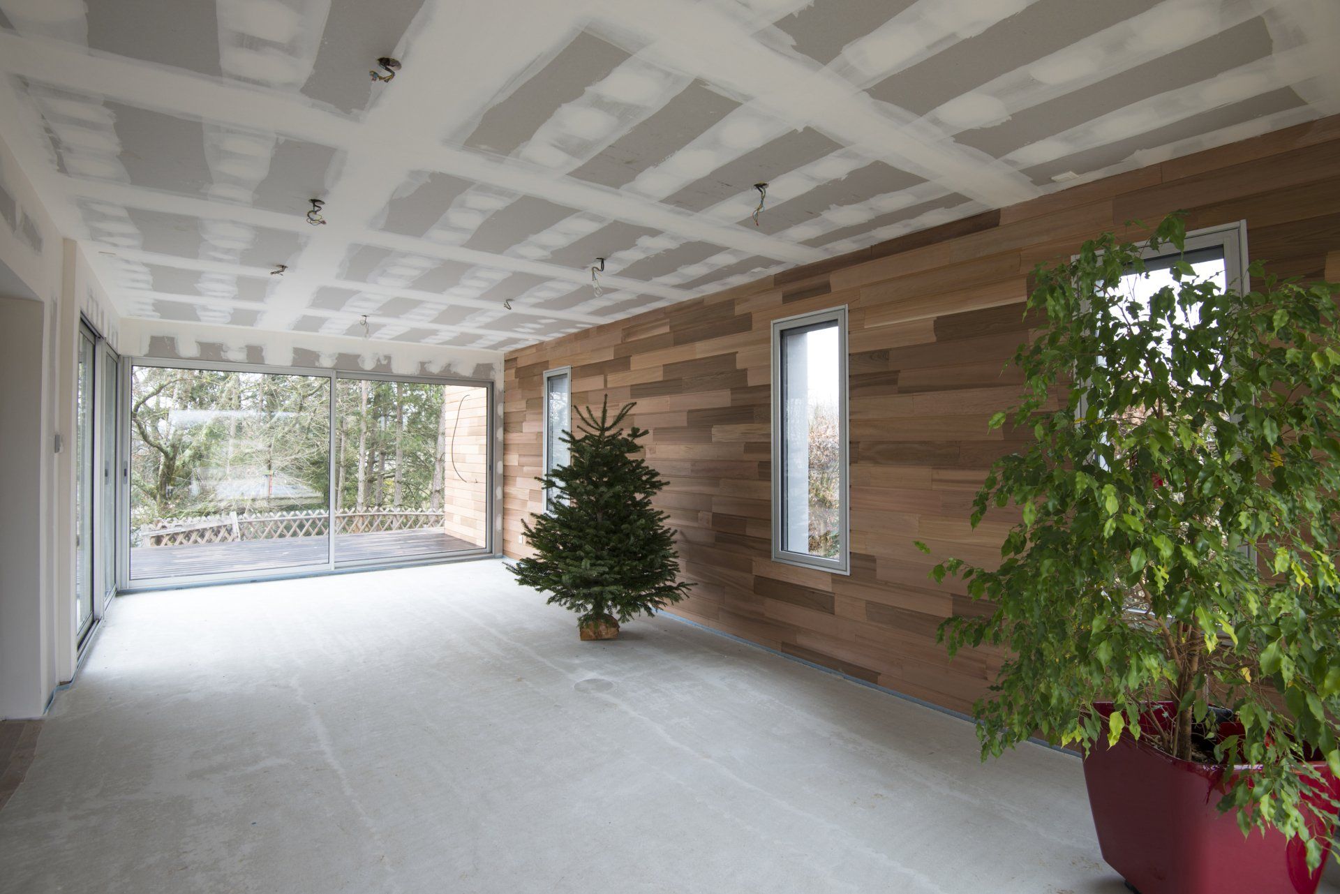 Chantier intérieur avec pose de placo au plafond, mur habillé en ossature bois, baie vitrée et sapin décoratif - chantier LC²
