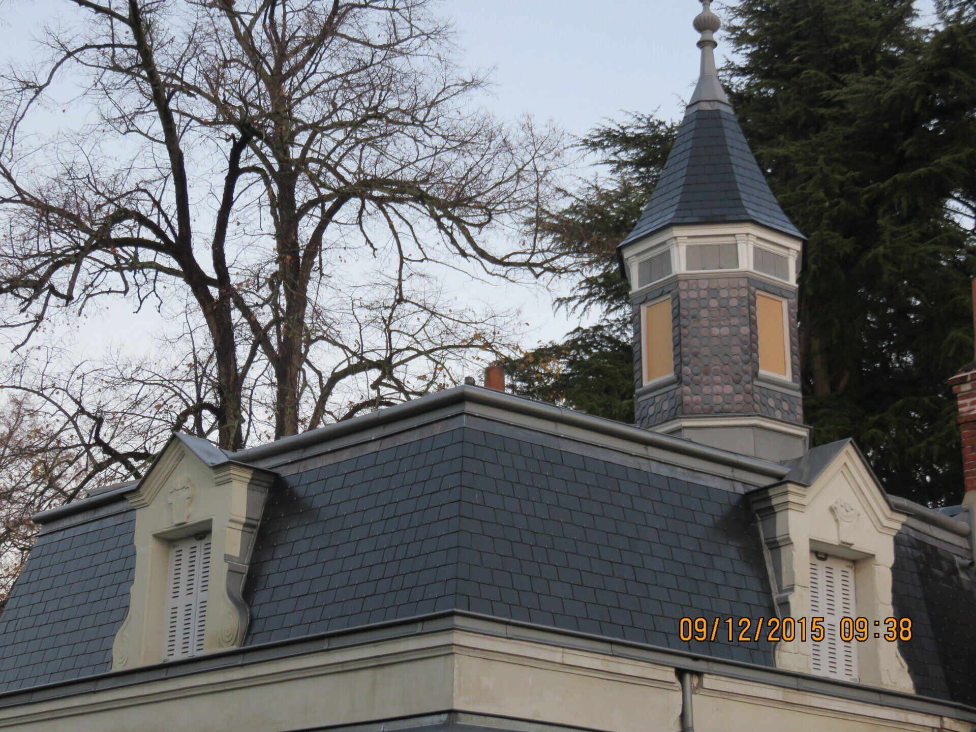 Toiture d'un bâtiment ancien avec un toit très pentu recouvert de bardeaux gris foncé et d'une tourelle