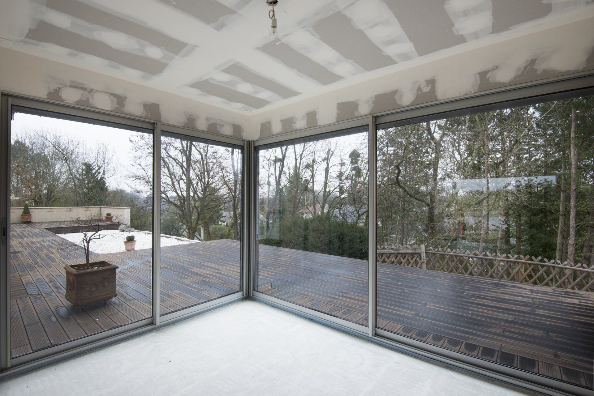Grande baie vitrée en angle avec vue extérieure sur la terrasse en bois