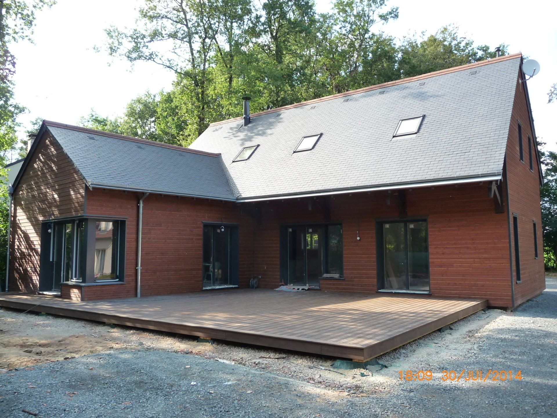 Maison en forme de L avec façade en bois, toiture en ardoise et une terrasse en bois 