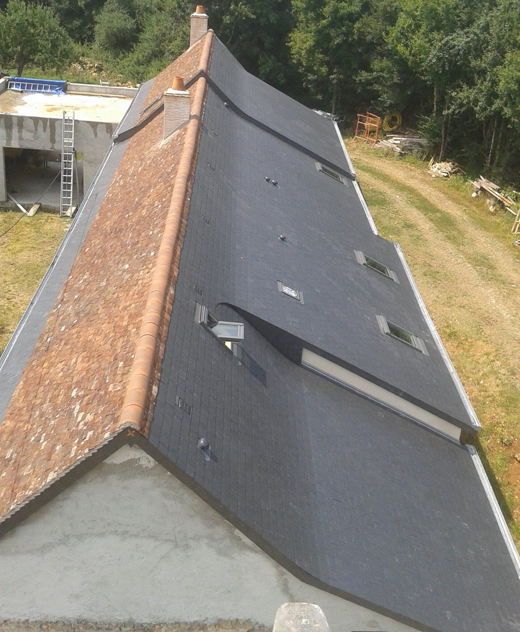 Toit mixte en ardoises foncées et tuiles rouges avec fenêtres de toit