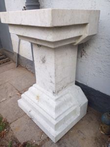 Auf dem Gehweg vor einem Gebäude steht ein weißer Steinsockel.