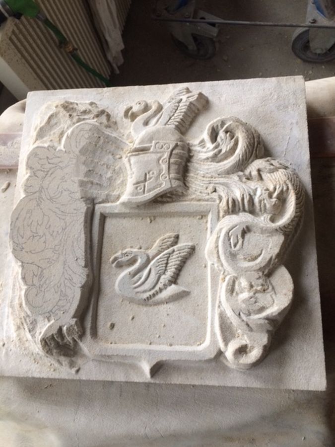 Auf einem Tisch steht eine Steinschnitzerei eines Wappens mit einem Schwan darauf.