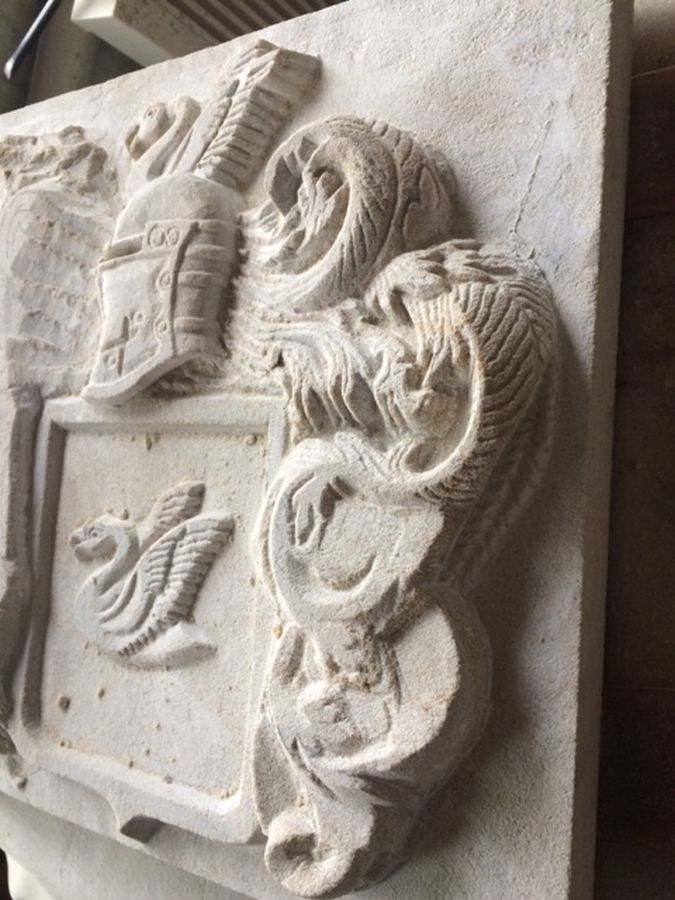 Eine Steinschnitzerei eines Ritterhelms und Schildes an einer Wand.