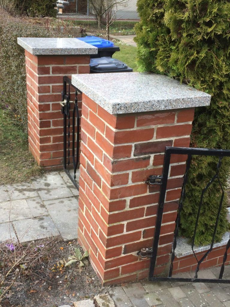 Eine Backsteinmauer mit einem Tor und Mülltonnen darauf.