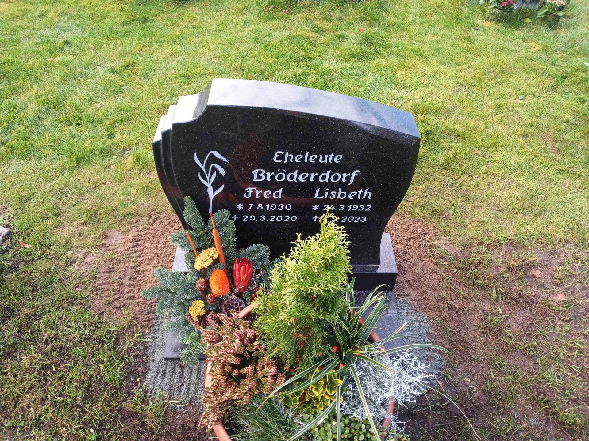 Ein schwarzer Grabstein mit Blumen darauf auf einem Friedhof.