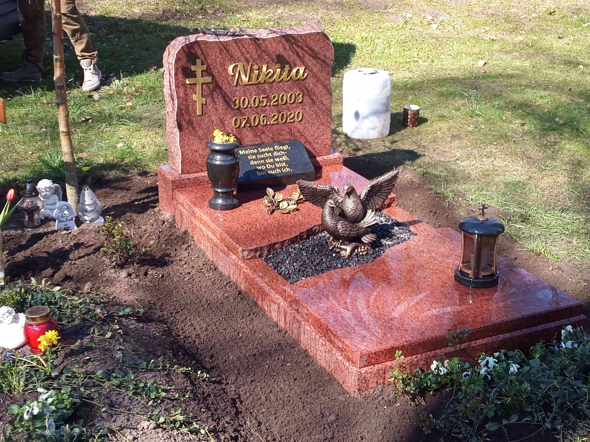 Ein roter Grabstein mit einem Vogel darauf auf einem Friedhof.