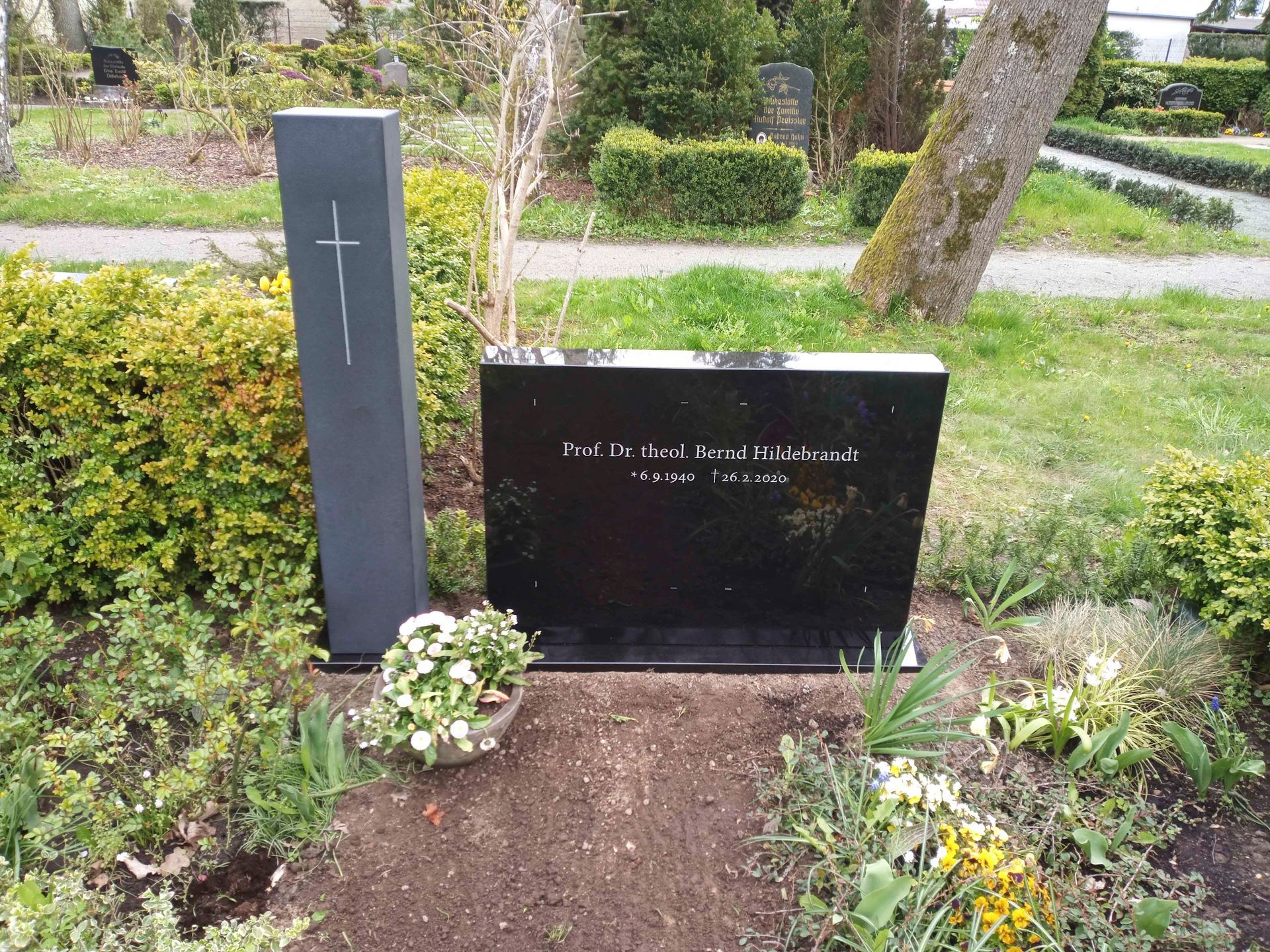 Ein schwarzer Grabstein auf einem Friedhof mit einem Kreuz darauf