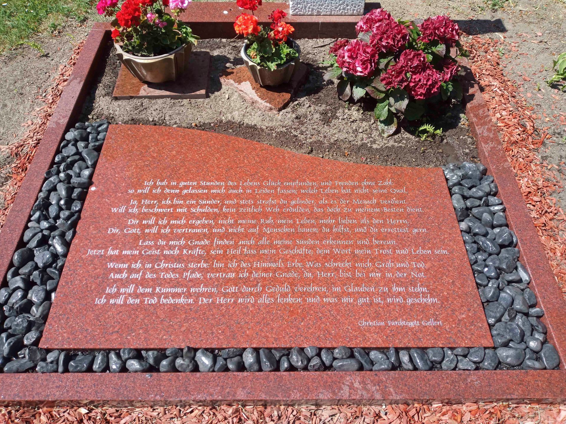 Ein Grab mit Blumen und Steinen auf einem Friedhof.