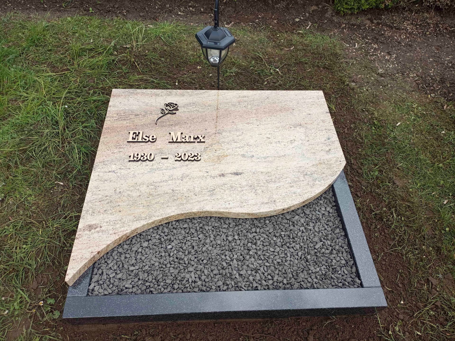 Ein Grabstein liegt im Gras neben einem Laternenpfahl.
