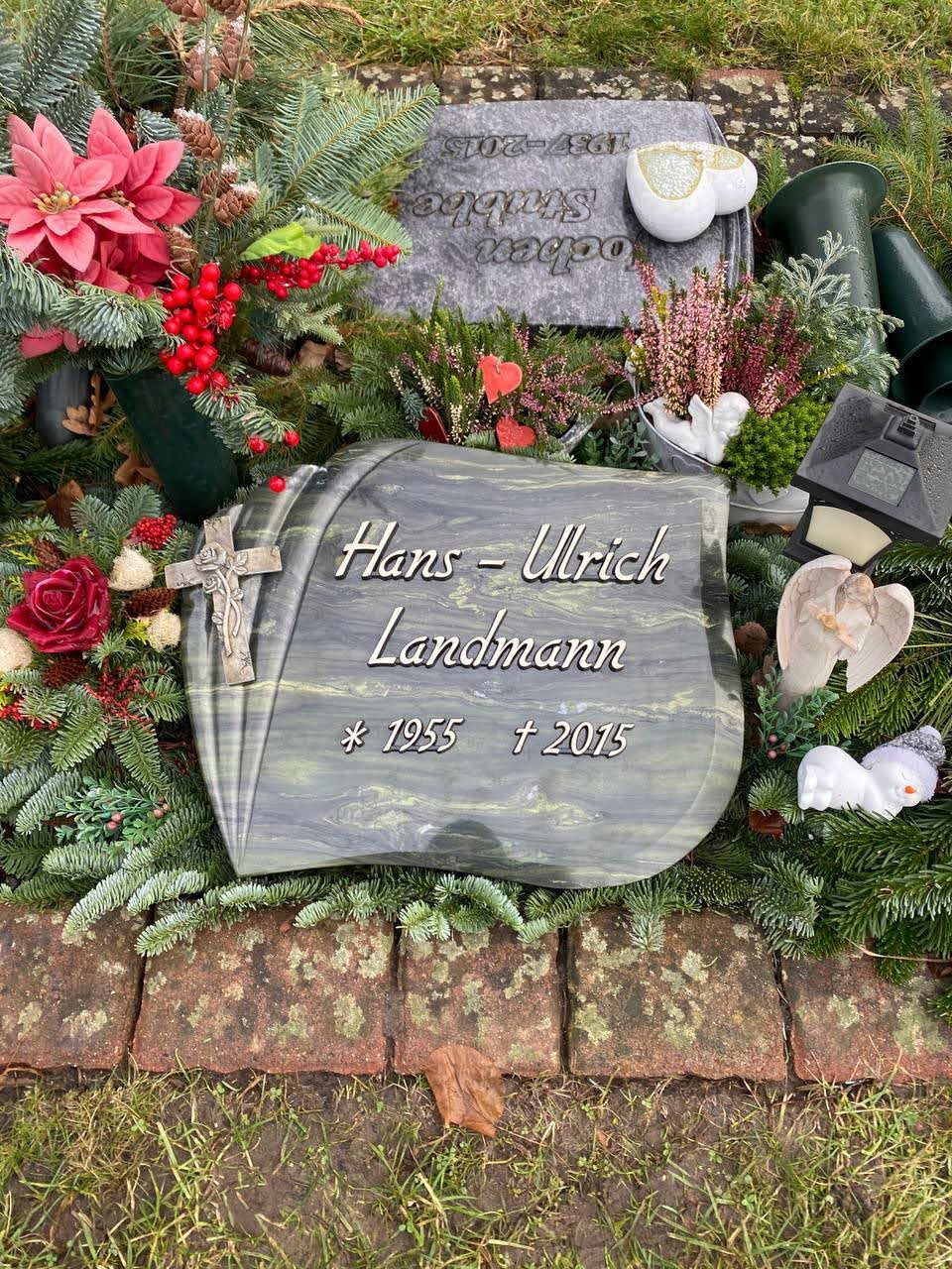 Ein Grabstein mit einem Kreuz und Blumen auf einem Friedhof.