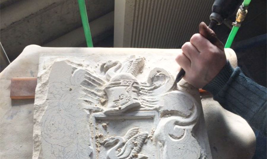 Eine Person meißelt ein Wappen in ein Stück Stein.