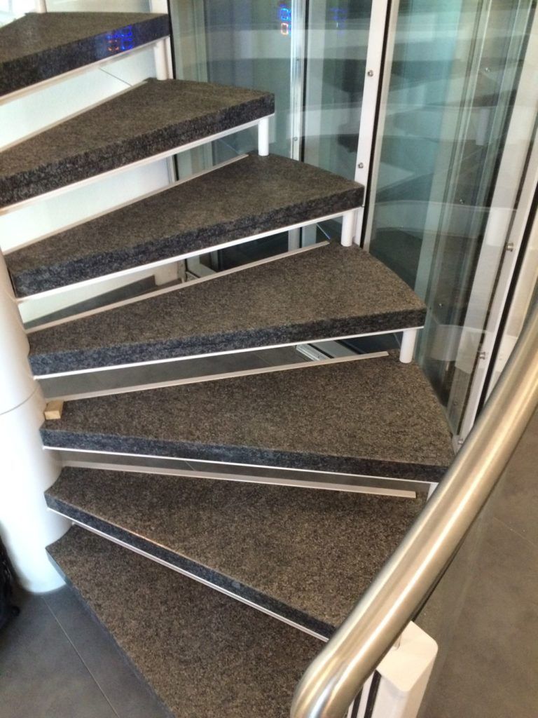 Eine Wendeltreppe mit mit Teppich ausgelegten Stufen und einem Geländer aus Edelstahl.